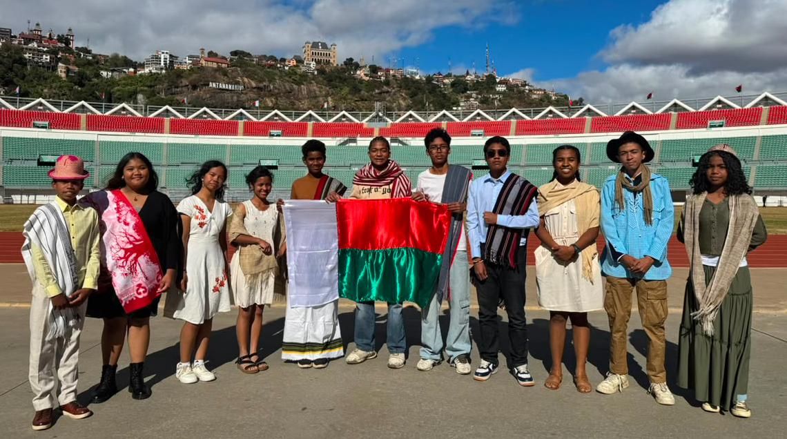 The eleven members of Team Madagascar in traditional Malagasy attire, holding the national flag at Barea Stadium in Antananarivo.